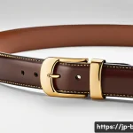 로에베 게이트 벨트와 퍼즐 벨트 스타일 - A close-up shot of a classic Loewe leather belt laid flat on a soft white fabric background, highlig...